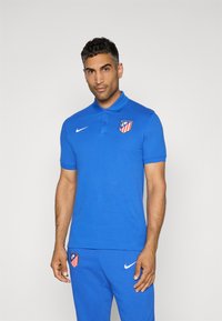 Blå polo t-shirt lavet af åndbart stof med krave, korte ærmer og et logo på brystet, kombineret med matchende blå bukser.