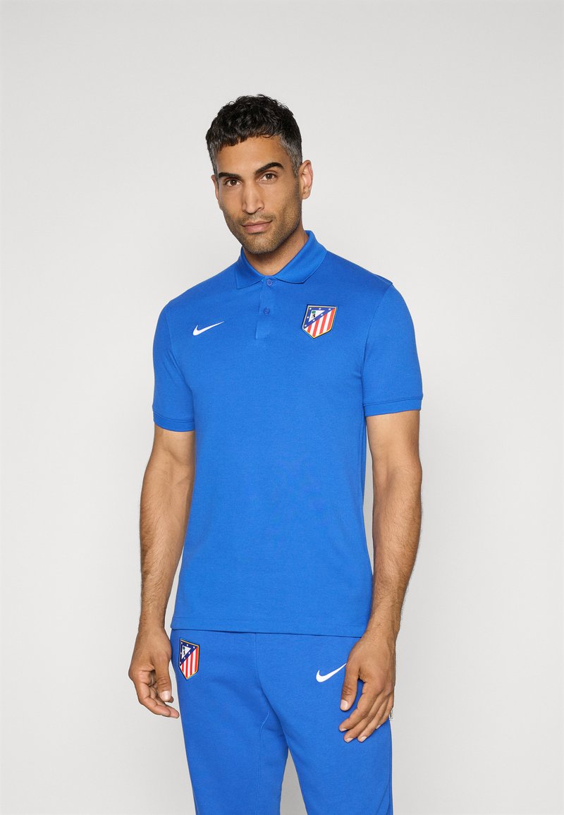 Blå polo t-shirt lavet af åndbart stof med krave, korte ærmer og et logo på brystet, kombineret med matchende blå bukser.
