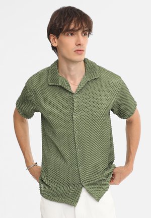 Chemise verte à manches courtes en tissu texturé avec un motif à pois, dotée d'un col et de boutons sur le devant.