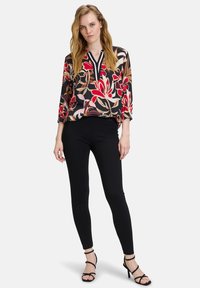 Bloemige blouse met een zwarte achtergrond, versierd met rode en crèmekleurige bloemen, en een V-halslijn. Gecombineerd met zwarte leggings en sandalen met bandjes.