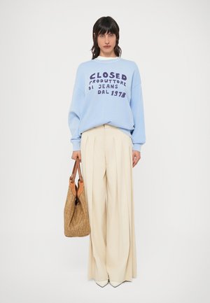 Ανοιχτογάλα μπουφάν με σκοτεινό μωβ κείμενο, κρεμ πλισέ παντελόνια και υφαντό τσάντα με καφέ λεπτομέρειες· καθαρές γραμμές, άνετη εφαρμογή.