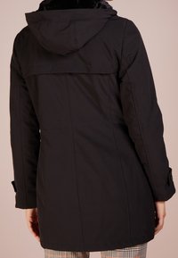 Svart parka jacka med en huva fodrad med päls, med rak passform, långa ärmar och knäppta manschetter. Slätt, matt tyg utan synliga mönster.