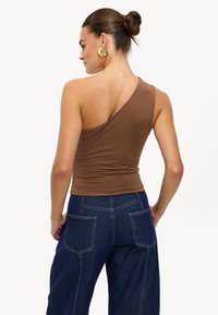 Haut marron à une épaule en tissu extensible, associé à un pantalon en denim bleu foncé taille haute avec des poches arrière et des coutures bien marquées.