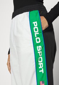 Byxor med elastisk midja och färgblockdesign i svart, vitt och grönt, med texten "POLO SPORT" och en amerikansk flagga som accent.