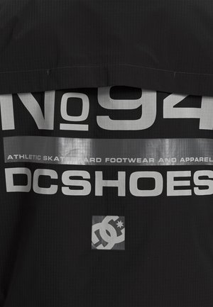 Czarna kurtka sportowa z dużym białym napisem: "No. 94" oraz "DC Shoes" z prostokątnym graficznym logo. Teksturowany materiał o delikatnym połysku.