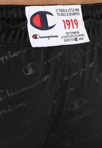 Svarta träningsshorts med mjuk textur, med ett subtilt mönster av "Champion"-logotyper över hela plagget och en märkestagg på midjebandet.