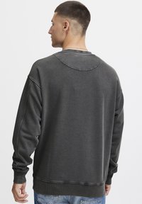 Sweatshirt noir à manches longues avec un col rond, des poignets et un ourlet côtelés. Tissu texturé avec des détails de couture visibles au dos.