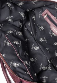 Wnętrze bordowej skórzanej torby z czarnym materiałowym wykończeniem. Wzór zawiera powtarzające się białe logo U.S. Polo Assn. oraz grafiki graczy polo.
