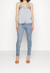 Grijze satijnen camisole met kanten details, gecombineerd met lichtblauwe skinny jeans met gouden geborduurde accenten. Transparante sandalen met bandjes.