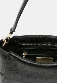 Sac à main en cuir noir avec une surface texturée, doté d'une fermeture éclair dorée, de poches intérieures et d'une courte bandoulière pour le porter.