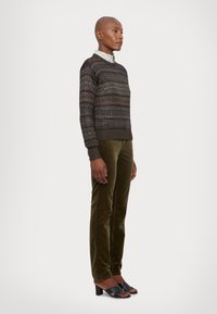 Knit sweater in dark brown with multicolored horizontal stripes, paired with olive green velvet pants and black heeled sandals.