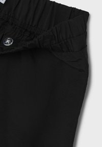 Pantalons noirs à taille élastique en tissu lisse, dotés d'une taille froncée et d'un seul bouton clair pour une fermeture sécurisée.