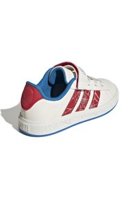 Weißer Sneaker mit roten Akzentstreifen, der ein Spinnennetzmuster aufweist, blauen Innenraum, Klettverschluss und runder roter Marken-Detail am Absatz.
