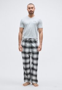 Grå V-hals T-skjorte med lett logo, kombinert med svart-hvite rutete flanellbukser. Myk tekstur, ledig passform, avslappet design, bare føtter.