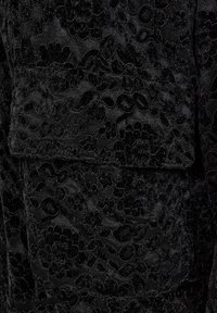 Svart tyg med ett tätt blommönster i sammet och en sydd rektangulär lappficka med klaff.