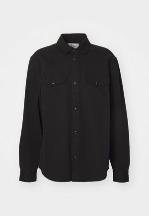 Zwarte langwerpige blouse, van katoen, met een puntige kraag, sluiting met knopen aan de voorkant, twee borstzakken met drukknoopsluiting, rechte onderkant, ontspannen pasvorm.