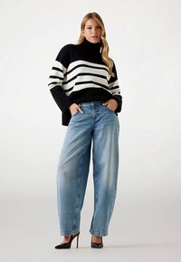 Čiernobiely pruhovaný rolák so uvoľneným strihom, skombinovaný so svetlo modrými džínsami s širokými nohavicami a čiernymi lodičkami na vysokom opätku.