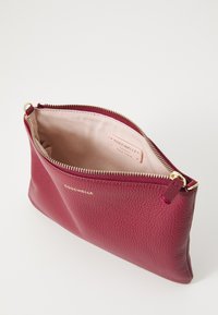 Burgundy leather clutch with a textured surface, gold zipper hardware, and a light pink fabric lining displaying the brand label inside.