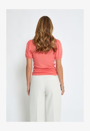 Koraljna rebrasta majica kratkih rukava, uskog kroja. Uparen s laganim kremastim hlačama širokih nogavica koje imaju glatku teksturu i stražnje džepove.