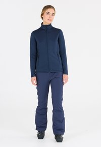 Marinblå zip-up jacka med ett texturerat mönster, tillsammans med matchande marinblå byxor. Outfiten har två sidofickor och en uppstående krage.