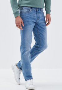 Hellblaue Jeans aus Denim mit geradem Schnitt, Fünf-Taschen-Design, dezenter Verwaschung an den Oberschenkeln und Nähdetails. Getragen mit weißen Sneakers.