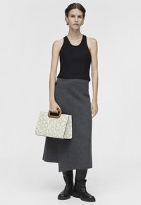 Czarny top na ramiączkach, szara wełniana spódnica, czarne kozaki do kolan oraz kremowa torba ze wzorem i drewnianym uchwytem. Prosty, strukturalny design.