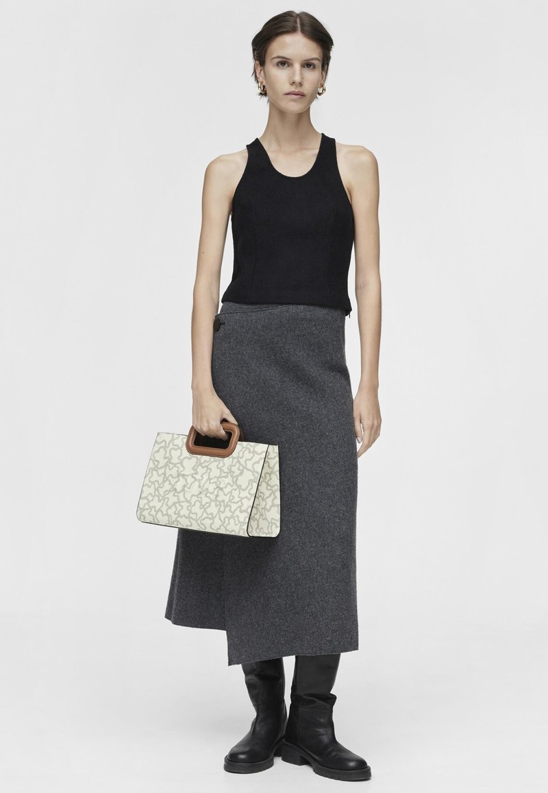Czarny top na ramiączkach, szara wełniana spódnica, czarne kozaki do kolan oraz kremowa torba ze wzorem i drewnianym uchwytem. Prosty, strukturalny design.