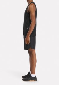Černé bezrukávové sportovní tričko v kombinaci s černými kraťasy; má prodyšnou tkaninu a elegantní design; nošeno s černými tréninkovými botami.