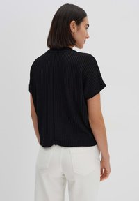 Schwarzes, geripptes Kurzarmoberteil mit entspannter Passform, rundem Halsausschnitt und abgerundetem Saum. Kombiniert mit weißen, hoch taillierten Hosen.