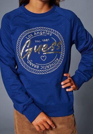 Blå sweatshirt i bomullsblandning med ribbade ärmar. Har en logotypdesign i guldglitter med repdetaljer och tryckt text.