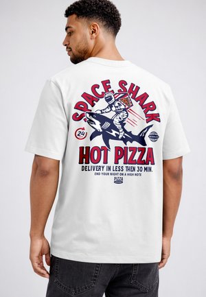 Man wearing white shirt with graphic of astronaut riding shark, holding pizza slice, and text promoting hot pizza delivery under 30 minutes.