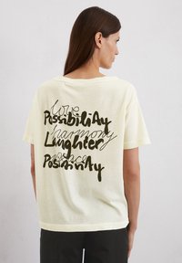Lichtgele relaxed-fit t-shirt met een zwart grafisch tekstontwerp op de achterkant, met verschillende handschrifttypes en zinnen. Zachte stof.