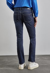 Mörkblå denimjeans med slim fit, försedda med två bakfickor och ljusa söndetails. Bärs ihop med vita sneakers.