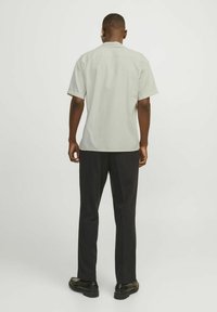 Light gray short-sleeve shirt with a classic collar, paired with black pants and black shoes, viewed from the back. Simple design, smooth texture.