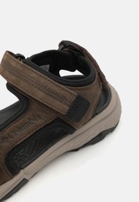 Brune tursandaler med borrelåsrem, strukturert overdel og en polstret såle. Har en mørk aksent og logodetalj på siden.