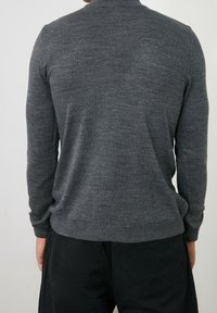 Grauer Pullover mit weichem Material, rundem Halsausschnitt und langen Ärmeln. Mit gerippten Bündchen und Saum, taillierte Passform. Getragen mit schwarzen Hosen.