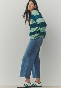Sweatshirt rayé vert et marine, coupe décontractée, associé à un jean large bleu clair et des baskets blanches avec des rayures vertes.