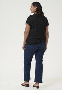 Zwarte, gestructureerde top met korte mouwen en een ronde hals, gecombineerd met donkerblauwe rechte jeans en zwarte blokhak-sandalen.