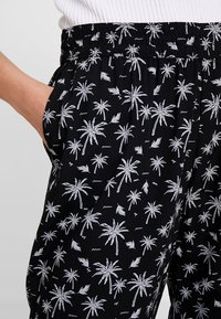 Pantalons noirs avec un motif de palmier blanc, taille élastique, poches latérales et une texture de tissu léger.