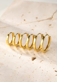 Złote kolczyki w formie obręczy ułożone w stos, o gładkiej fakturze i błyszczącym wykończeniu, o różnej wielkości od małych do dużych.