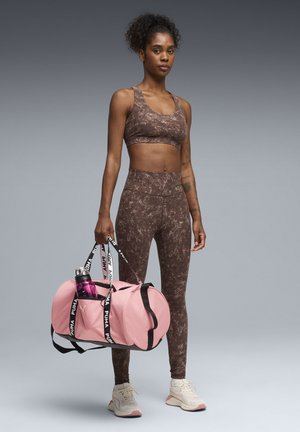 Brun mønstret sports-bh og leggings kombineret med en lyserød sportstaske med sorte stropper. Tasken indeholder en vandflaske. Lyse sneakers.