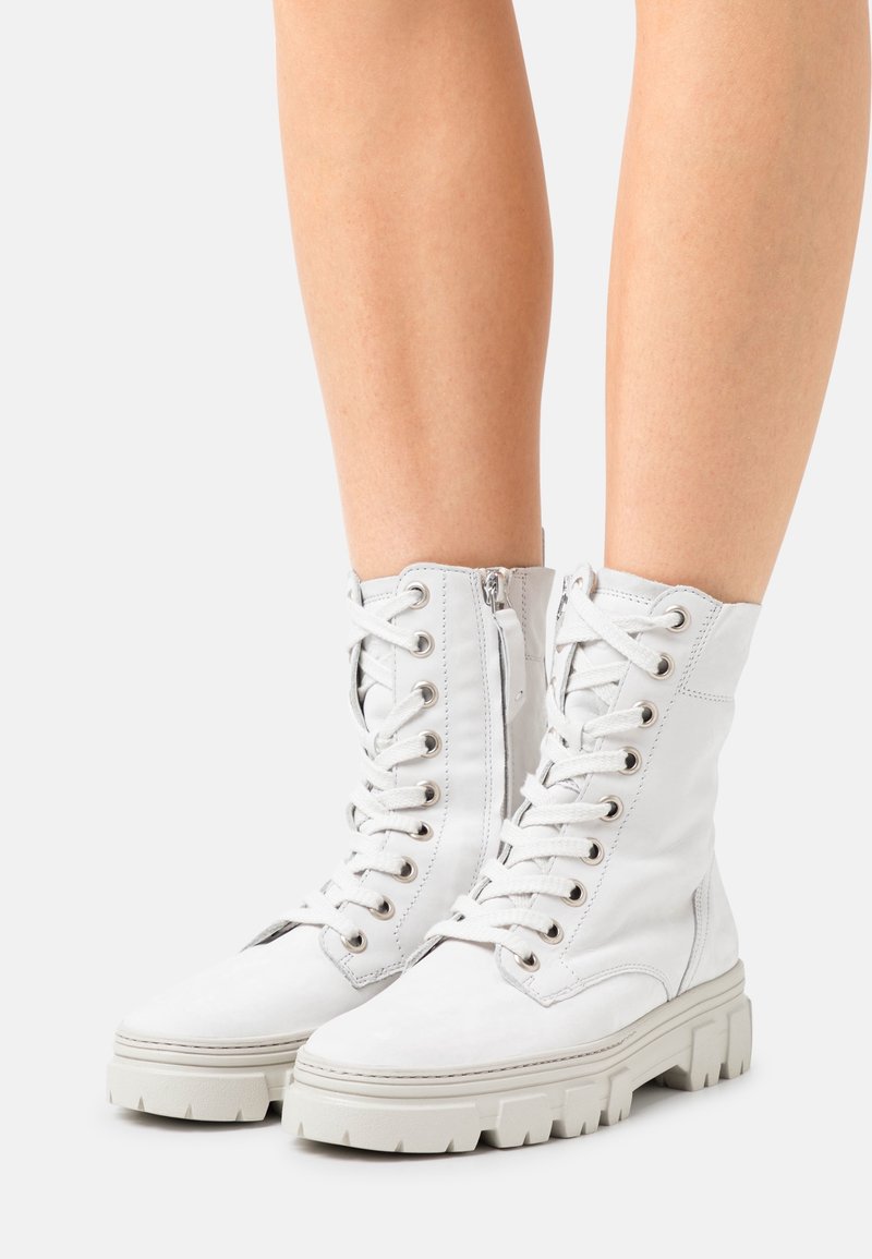 Botas de combate altas blancas hechas de cuero suave, con suelas de goma gruesas, cordones con ojales y una cremallera lateral para ponerlas y quitarlas con facilidad.