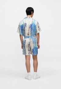 Kratek večbarven romper z rokavi do komolcev v modro-belo-fialnem abstraktnem vzorcu; elastični pas; sproščen kroj; dolžina nad koleni.