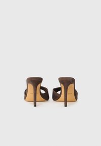 Une paire de mules à talons hauts en suede marron avec des open backs et des talons aiguilles pointus sur fond blanc.