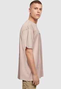 Lys pink bomulds t-shirt med korte ærmer, rund halsudskæring og en afslappet pasform. Har et diskret grafisk print på forsiden og bagsiden.