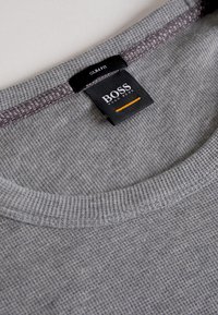 Graues Slim-Fit-Hemd mit strukturierter Stoffqualität, rundem Ausschnitt und dunklem Saum. Etikett mit der Aufschrift "BOSS" und orangefarbenem Akzent.