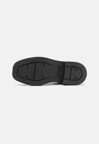Black rubber shoe sole with textured finish, featuring a distinctive tread pattern and engraved brand logo on the side.