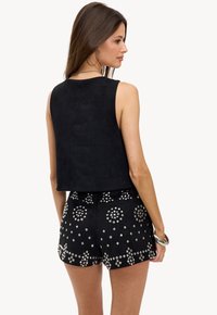 Haut cropped en suède noir associé à un short noir avec des accents en studs argentés étincelants dans un motif géométrique.