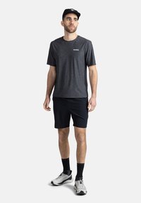 Šedé sportovní tričko s krátkým rukávem a logem, doplněné černými šortkami. Bílé tenisky a černé ponožky dokončují sportovní vzhled.