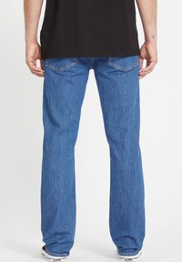 Jeans de denim azul con un corte recto, que cuentan con bolsillos traseros, una textura deslavada y un diseño clásico. Combinados con zapatillas negras.